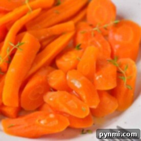 Sliced and glazed carrots with herbs are elegantly arranged on a white plate beside a fork, offering a perfect example of how to cook carrots to enhance their natural sweetness.