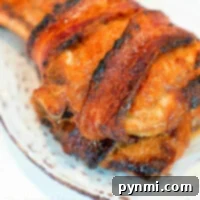 Air fryer pork chop recipe inspiration: enjoy bacon-wrapped chicken breast on a white speckled plate, showcasing a crispy, golden-brown texture.