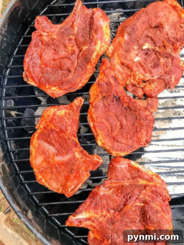 Five seasoned pork chops, perfectly prepared with a flavorful dry rub, are lined up on the grill, ready for cooking.