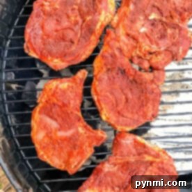 Five seasoned pork chops, perfectly prepared with a flavorful dry rub, are lined up on the grill, ready for cooking.