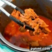 Tongs carefully lift tender beef from an Instant Pot filled with rich, red sauce, embodying the essence of classic beef roast recipes.