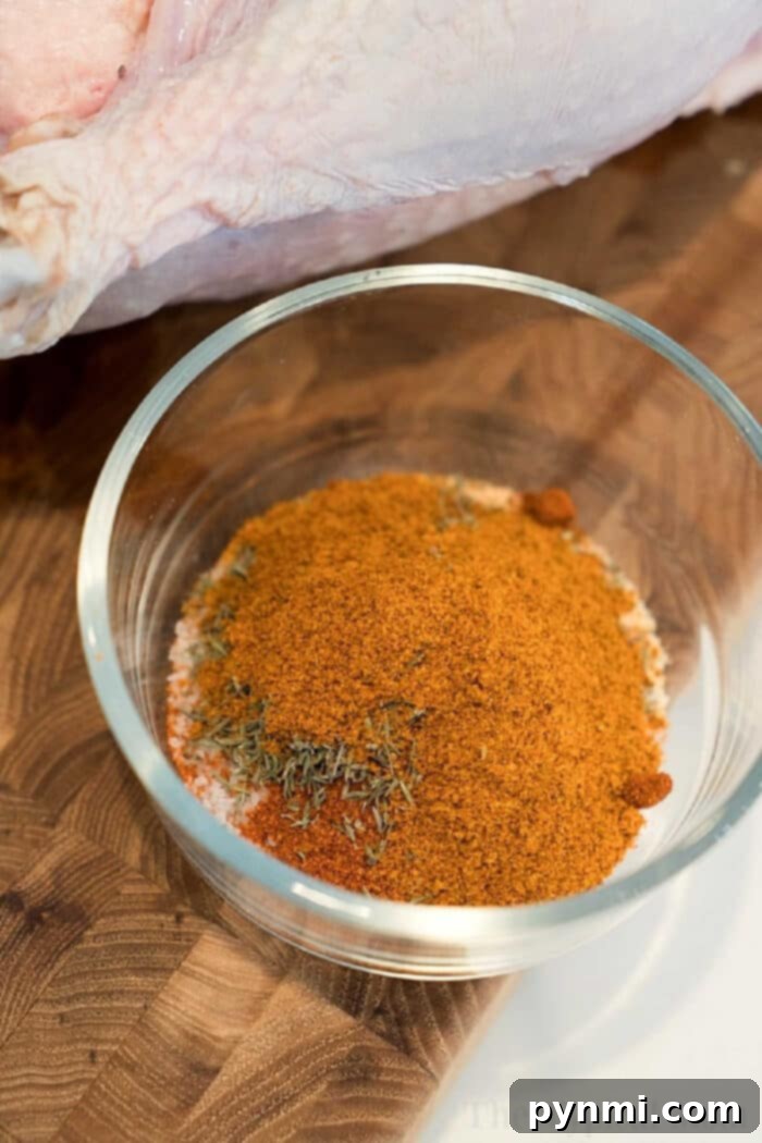 A glass bowl filled with a mix of dry spices for a smoked turkey rub recipe sits on a wooden surface next to raw poultry.