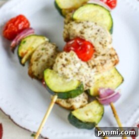 Air fryer chicken kabobs with zucchini, cherry tomatoes, and red onion arranged beautifully on a white plate.