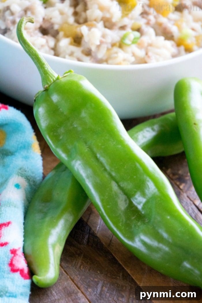 Fresh hatch green chili peppers rest on a wooden surface, hinting at the spicy twist in your instant pot sausage rice casserole, with a bowl of cooked rice in the background.