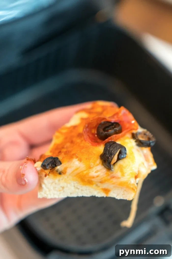 Freshly cooked pepperoni pizza being removed from an air fryer.