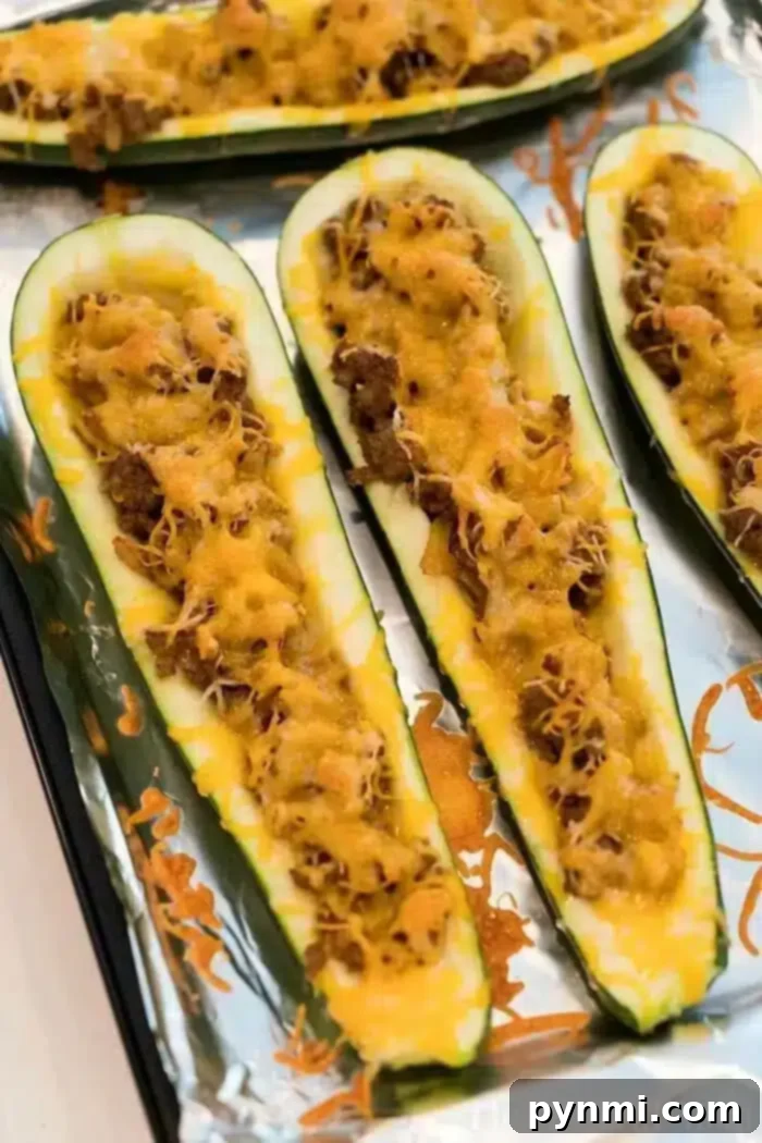 Air fryer zucchini boats topped with ground meat and melted cheese are lined on a foil-covered baking sheet.