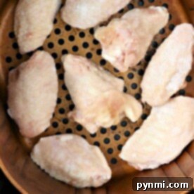 Frozen chicken wings perfectly arranged in a single layer in an air fryer basket, ensuring even cooking.