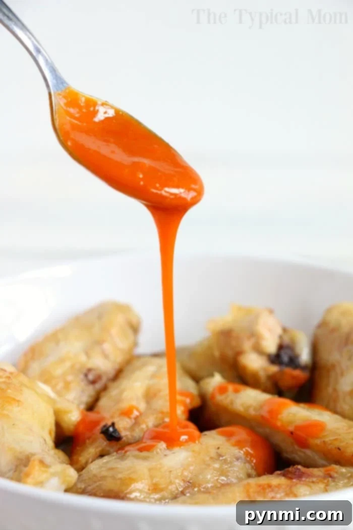 Crispy Air Fryer Frozen Chicken Wings 7 Spoon drizzling bright orange sauce over a bowl of crispy chicken wings straight from the air fryer.