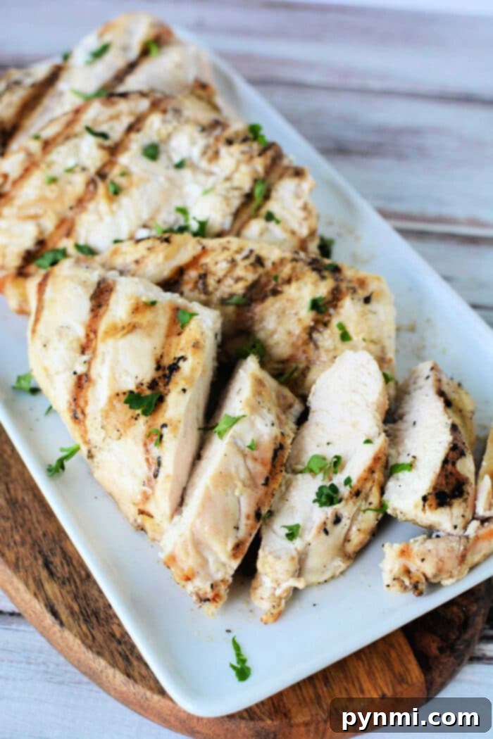 Crispy Air Fryer Frozen Chicken Breasts 6 Sliced frozen chicken breast cooked to perfection in an air fryer, elegantly displayed on a white platter and garnished with fresh chopped herbs.