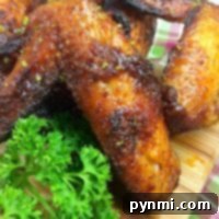 Close-up of seasoned, roasted chicken wings on a wooden cutting board, garnished with fresh parsley. These air fryer wings boast crispy perfection. In the background, part of a plaid cloth is visible.