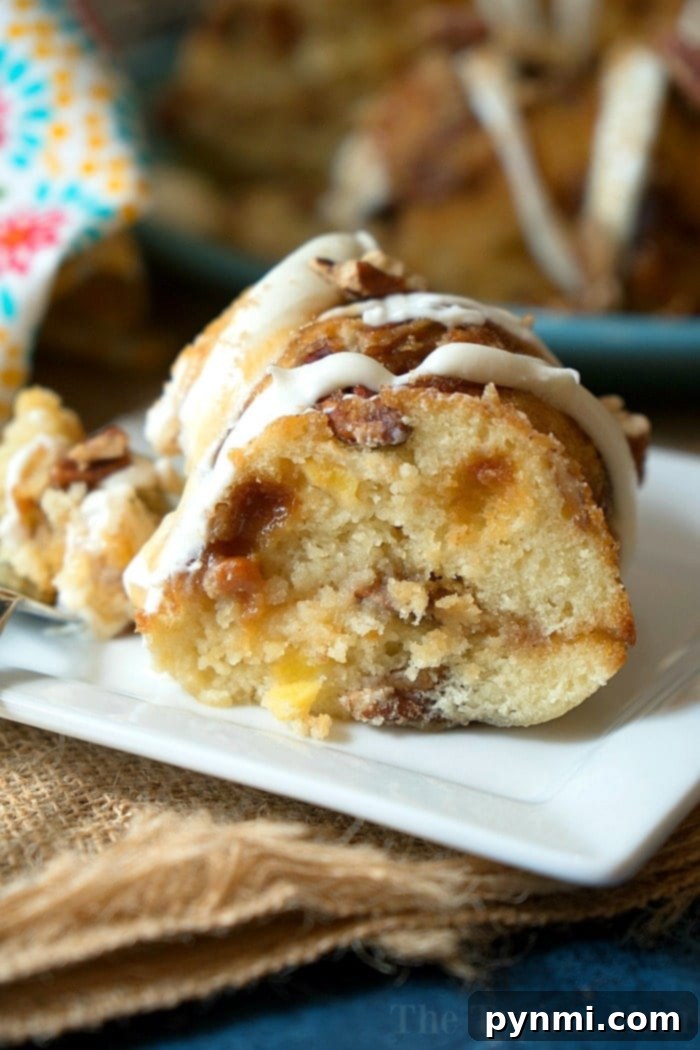 Instant pot baking. #instantpot #coffeecake #breakfast #instantpotrecipes #august #summer #seasonal #fruit #vegetable A slice of glazed bundt cake with nuts sits elegantly on a white plate, its presentation as inviting as any August Instant Pot recipe, all resting on rustic burlap fabric.