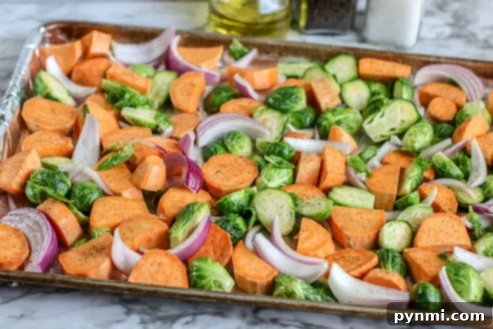 One-Pan Crispy Chicken Thighs 4 A vibrant mix of sheet pan vegetables, including sweet potatoes, brussels sprouts, and red onion, ready for roasting.