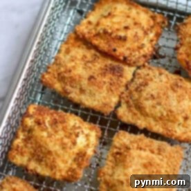 Eight pieces of breaded, golden-brown air fryer ravioli rest on a wire rack placed over a baking tray.