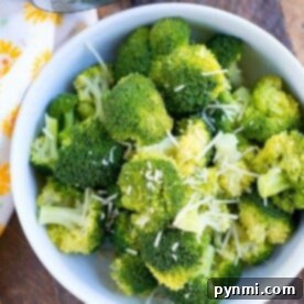 A bowl filled with freshly cooked broccoli florets, sprinkled with grated cheese, makes a perfect instant pot side dish. Positioned on a wooden surface next to your trusty Instant Pot pressure cooker, it sits elegantly beside a white cloth adorned with yellow flowers.