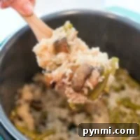 A hand gracefully serves a delightful instant pot cream of mushroom rice dish from a pot with a wooden spoon.