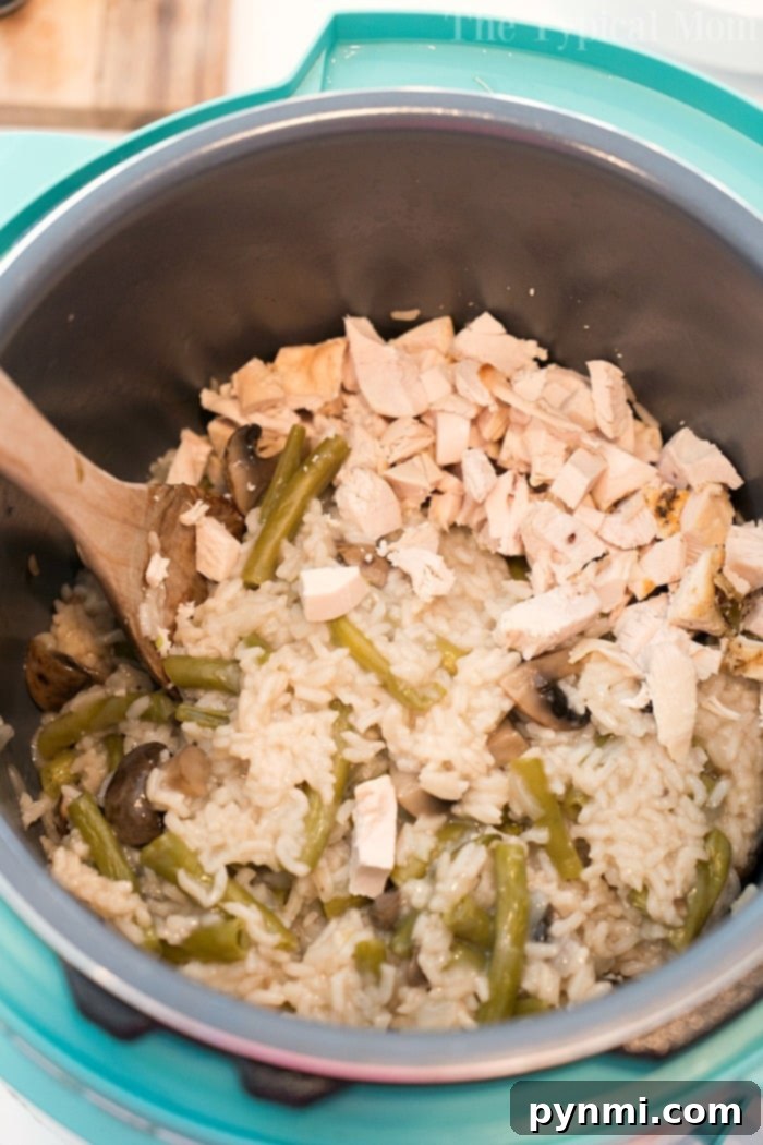 Rice with green beans, mushrooms, and tender chicken pieces in a pressure cooker, stirred with a wooden spoon, showcasing the delicious blend of ingredients.