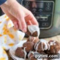 Fluffy Air Fryer Donut Bites 9 A hand holds an iced air fryer donut made with cinnamon rolls, with the trusty ninja foodi in the background.