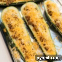 Loaded Zucchini Taco Boats 5 Zucchini taco boats stuffed with seasoned ground meat and topped with shredded cheese rest invitingly on a foil-lined tray.