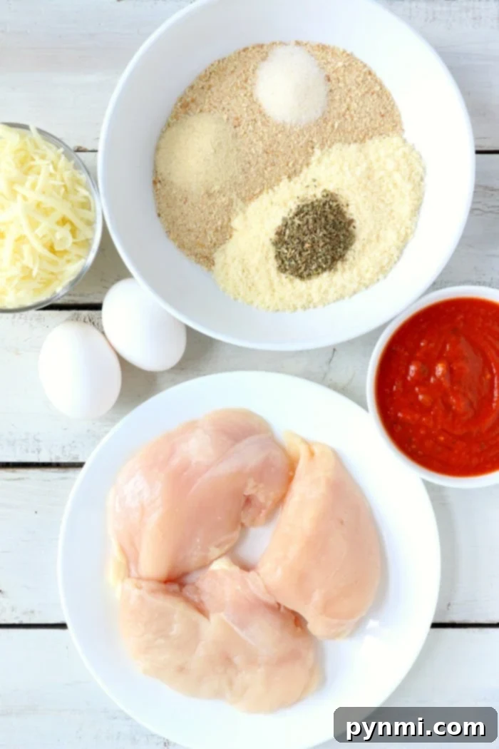Bowls of ingredients for crafting delicious air fryer chicken parm. Bowls of ingredients on a white surface include raw chicken breasts, breadcrumbs with herbs and spices, marinara sauce, grated cheese, and two eggs—perfect for crafting delicious air fryer chicken parm.
