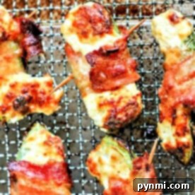Close-up of bacon-wrapped jalapeño poppers with melted cheese, fresh from the air fryer, resting on a wire rack.