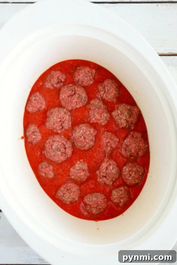 Slow cooker spaghetti is a game changer! NO need to boil noodles when making this pasta dinner in your slow cooker. Homemade comfort food. #crockpot #spaghetti #slowcooker #crockpotspaghetti #spaghettiandmeatballs Crockpot meatballs simmering in rich tomato sauce.