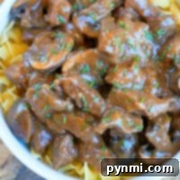 Instant Pot beef tips stroganoff with mushrooms, served over egg noodles and garnished with chopped herbs in a white bowl.