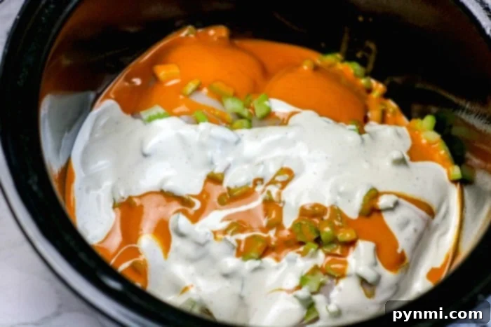 Flavor-Packed Slow Cooker Buffalo Sliders 4 A vibrant close-up of slow cooker buffalo chicken, shredded and coated in a rich, orange sauce, ready to be assembled into sliders.