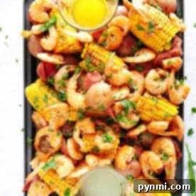 A tray of instant pot shrimp boil with corn, potatoes, sausage, herbs, and two bowls of dipping sauces.