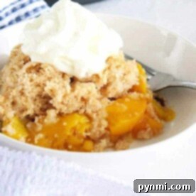 A bowl of instant pot peach cobbler crowned with whipped cream, with a fork waiting eagerly by the side.