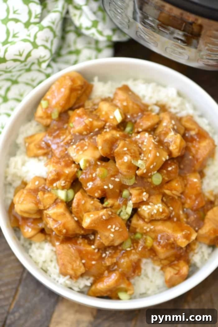 A bowl of sesame chicken with a savory sauce over white rice, garnished with green onions, is a perfect dish to try from Septembers Instant Pot recipes.