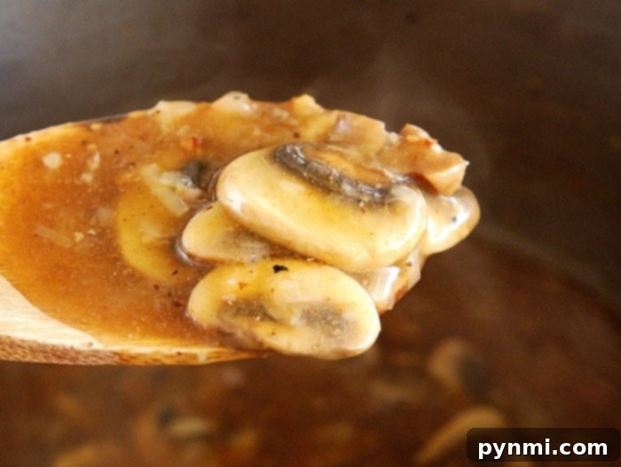 Effortless Instant Pot Salisbury Steak 6 Close-up of mushrooms in a rich brown sauce, reminiscent of Instant Pot Salisbury steak, on a wooden spoon.