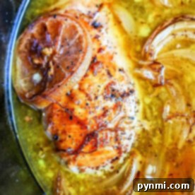 Close-up of crockpot lemon pepper chicken with caramelized onions simmering in a savory broth.