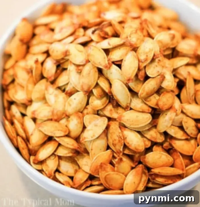 A white bowl filled with a large quantity of seasoned, roasted air fryer pumpkin seeds. The seeds appear golden brown and are seasoned with various spices.