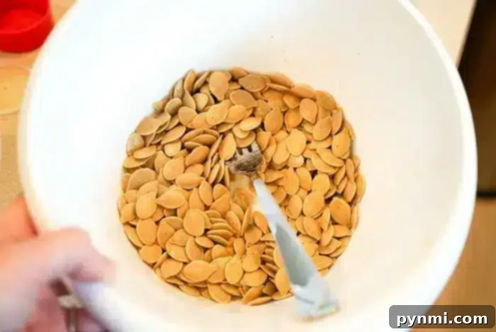 A white bowl filled with a generous amount of air fryer pumpkin seeds is shown. A fork is resting in the bowl, partially covered by the seeds. The image focuses on the tan-colored seeds, which are evenly spread out in the bowl.