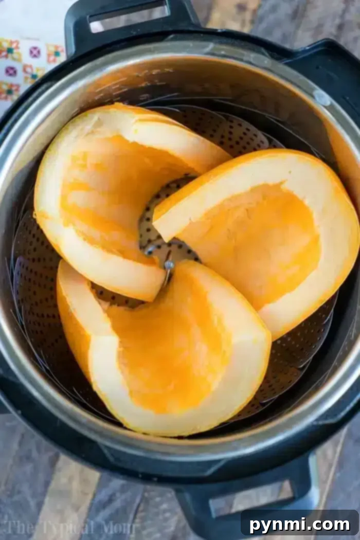 Three pumpkin slices rest inside an Instant Pot with a steamer basket, perfect for October's cozy recipes. Cut into large wedges, they showcase their bright orange flesh. The pot sits invitingly on a wooden surface.