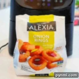 A bag of Alexia crispy frozen onion rings sits in front of an air fryer on a white countertop, ready to be cooked to perfection.