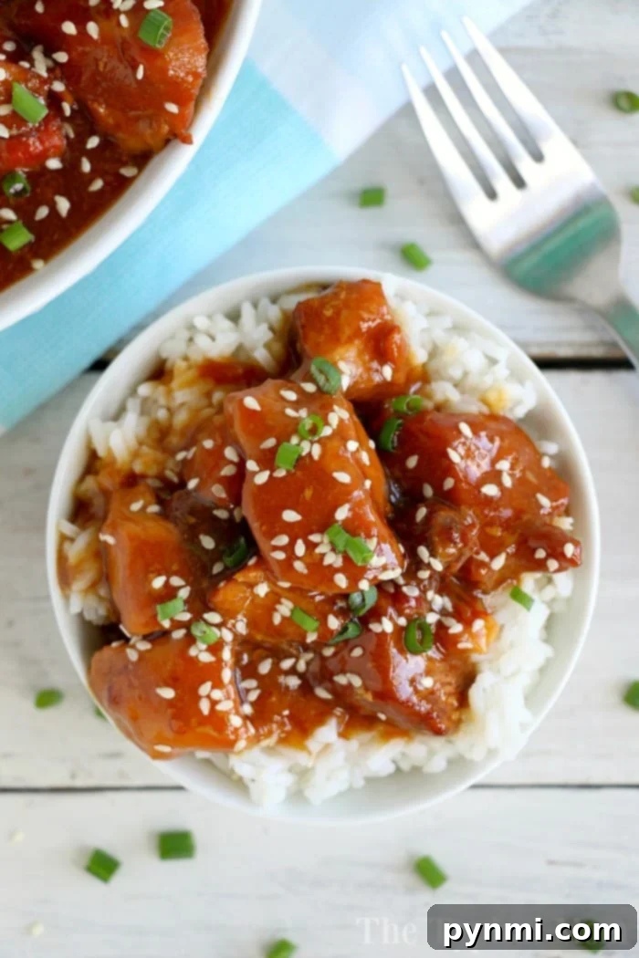 Crockpot sesame chicken recipe is here! Sticky honey sweet chicken thighs or breasts with a kick served on top of a bed of rice will be your favorite slow cooker meal. #crockpot #crockpotrecipes #sesamechicken #chicken #crockpotchicken #honey Hearty slow cooker sesame chicken with garnishes.