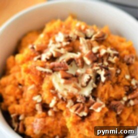 Creamy mashed sweet potatoes, perfectly cooked, topped with melting butter and chopped pecans, served in a white bowl.