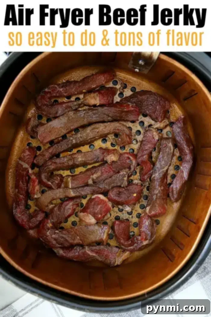 A metal air fryer basket is filled with pieces of savory beef jerky. The top of the image contains text that reads: "Air Fryer Beef Jerky so easy to do & tons of flavor." The setup is on a gray-patterned countertop.