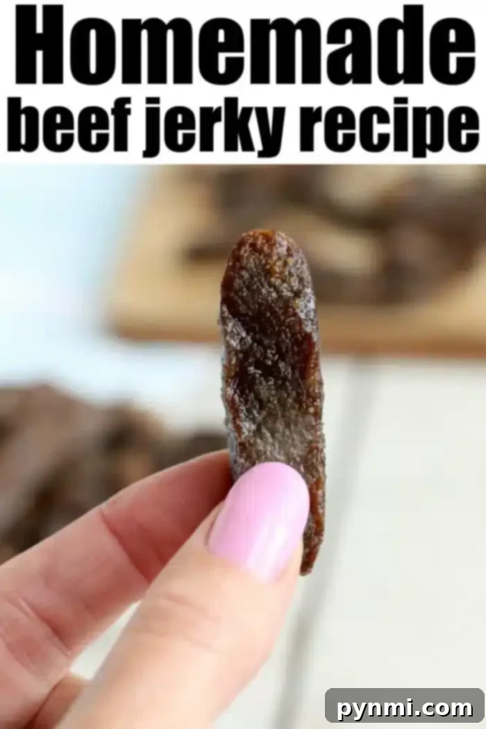 A close-up of a hand with pink-painted nails holding a piece of beef jerky. "Homemade air fryer beef jerky recipe" is written in bold black letters at the top of the image. In the background, more pieces of jerky are spread out on a wooden surface.
