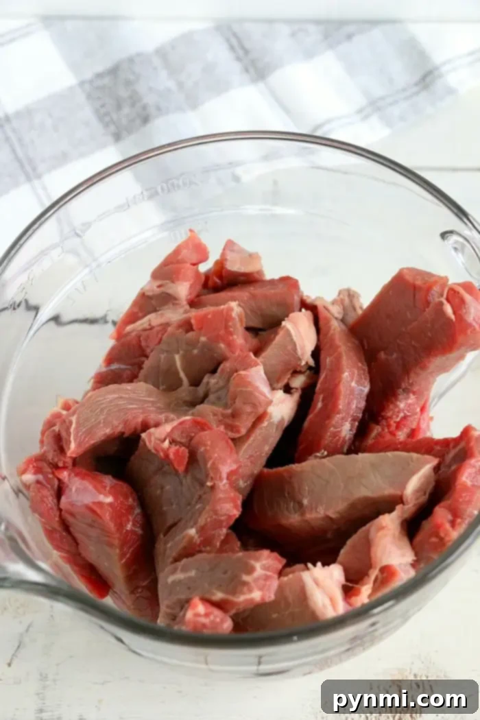 A clear glass bowl filled with raw, thinly sliced beef pieces, perfect for making air fryer beef jerky.