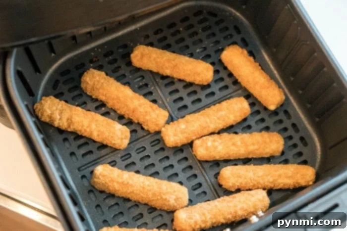 A close-up of golden, crispy frozen mozzarella sticks in an air fryer basket, ready to be removed.