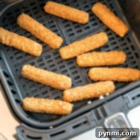 Frozen mozzarella sticks are neatly arranged in an air fryer basket, ready to be cooked.