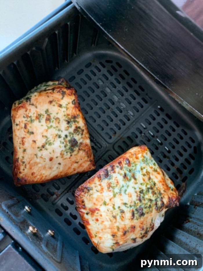 Two seasoned pork fillets sit in an air fryer basket, lightly browned and sprinkled with herbs. For a hearty twist, use this method to prepare an air fryer pork loin as well.