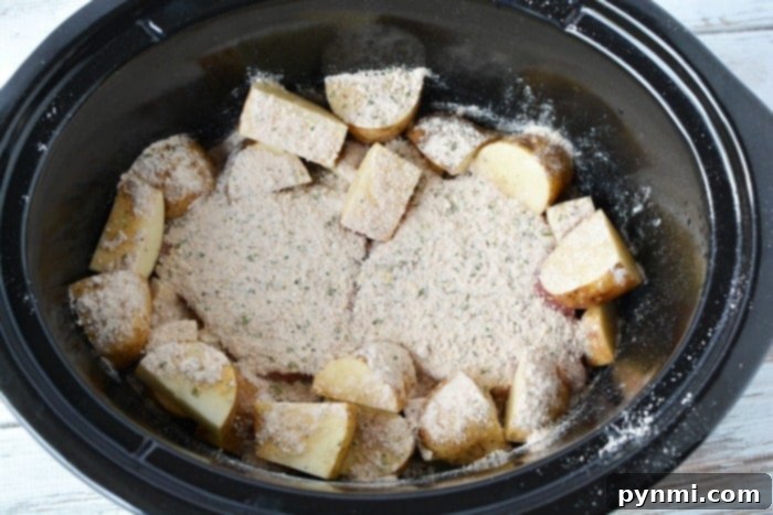 Sliced potatoes with seasoning nestle alongside tender crockpot steak in a black slow cooker.