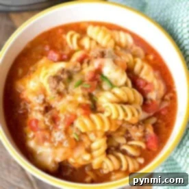 A bowl of rotini pasta with savory meat sauce and melted cheese sits enticingly on a wooden surface next to a green cloth, evoking the comforting flavors of an instant pot enchilada casserole.