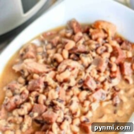 A bowl of black-eyed peas with chunks of meat in a savory broth, perfectly crafted from a tried-and-true crockpot black-eyed peas recipe, sits invitingly beside the slow cooker.