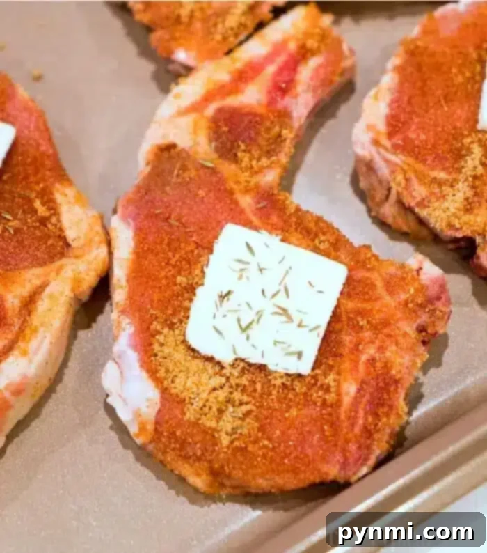 The best baked pork chops are seasoned with spices and carefully arranged on a baking tray. Each succulent chop boasts a pat of butter on top, enhanced with a sprinkle of dried herbs for perfect flavor.