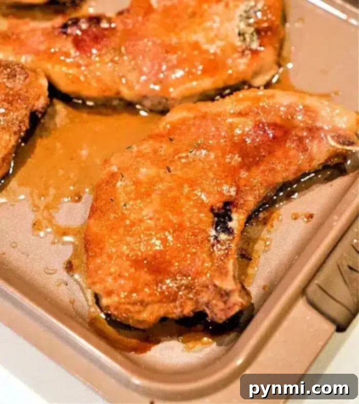 The best baked pork chops rest on a metal baking sheet, glistening with juices and lightly browned on the edges.