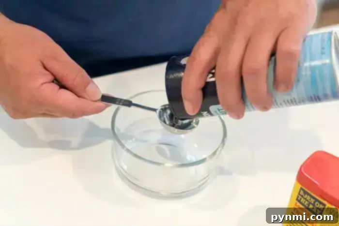 A person carefully measures salt from a red-lidded container into a measuring spoon, poised above a small glass bowl on a white surface, perfect for enhancing the flavors of the best baked pork chops.